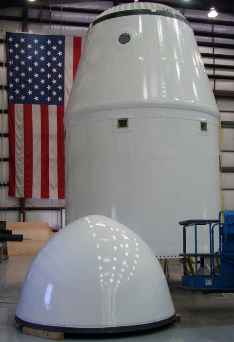 Pressurized portion of the Dragon spacecraft, top, mated to the cylindrical unpressurized trunk section below. As Dragon has been designed from the start for human transport, even the cargo and demonstration versions include windows (circle at top, covered for protection during painting). Photo credit: SpaceX. Pressurized portion of the Dragon spacecraft, top, mated to the cylindrical unpressurized trunk section below. As Dragon has been designed from the start for human transport, even the cargo and demonstration versions include windows (circle at top, covered for protection during painting). Photo credit: SpaceX.