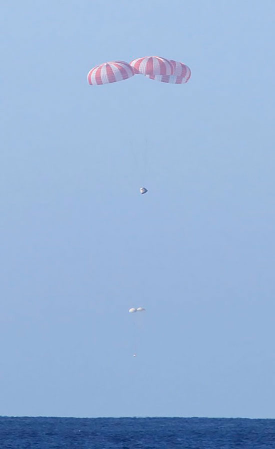 Dragon’s three main parachutes fully deployed. Below float two drogue parachutes which deployed first to slow and stabilize the spacecraft. Dragon’s three main parachutes fully deployed. Below float two drogue parachutes which deployed first to slow and stabilize the spacecraft.