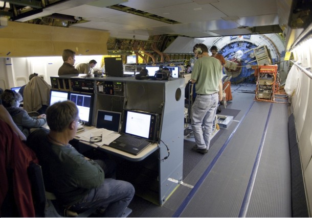During a science flight aboard SOFIA. View aft on main deck shows mission operations and science team personnel and consoles. The scientific instrument (red cylinder) is mounted on the flange at upper right. The telescope itself is behind the pressure bulkhead at the end of the cabin. Image credit: NASA/DLR/USRA/DSI/FORCAST team During a science flight aboard SOFIA. View aft on main deck shows mission operations and science team personnel and consoles. The scientific instrument (red cylinder) is mounted on the flange at upper right. The telescope itself is behind the pressure bulkhead at the end of the cabin. Image credit: NASA/DLR/USRA/DSI/FORCAST team