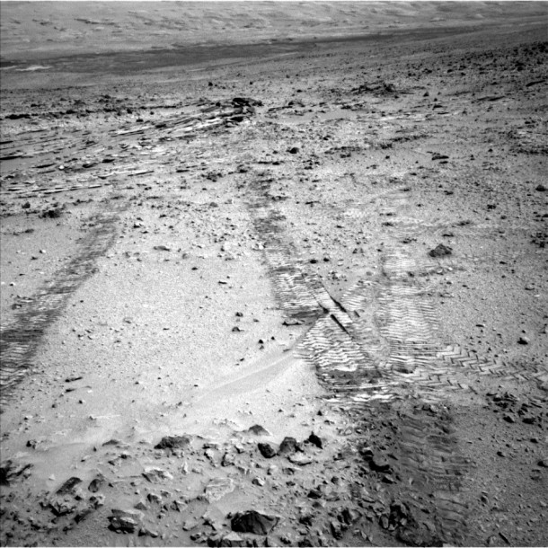 This view from the left Navigation Camera (Navcam) of NASA's Mars Rover Curiosity looks back at wheel tracks made during the first drive away from the last science target in the "Glenelg" area. The drive commenced a long trek toward the mission's long-term destination: Mount Sharp. Curiosity drove 59 feet (18) meters on the 324th Martian day, or sol, of the rover's work on Mars. It took this image that same sol, looking back toward the target sedimentary outcrop called "Shaler." Wheel tracks in the right foreground of the image were left by Curiosity's earlier passage through this area on its way toward Glenelg targets seven months earlier. Credit: NASA/JPL-Caltech This view from the left Navigation Camera (Navcam) of NASA's Mars Rover Curiosity looks back at wheel tracks made during the first drive away from the last science target in the "Glenelg" area. The drive commenced a long trek toward the mission's long-term destination: Mount Sharp. Curiosity drove 59 feet (18) meters on the 324th Martian day, or sol, of the rover's work on Mars. It took this image that same sol, looking back toward the target sedimentary outcrop called "Shaler." Wheel tracks in the right foreground of the image were left by Curiosity's earlier passage through this area on its way toward Glenelg targets seven months earlier. Credit: NASA/JPL-Caltech