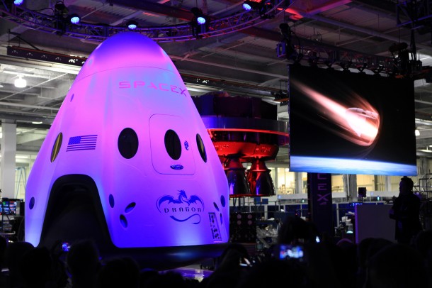 An artist concept video of the Dragon V2 re-entering Earth's atmosphere plays alongside the newly unveiled spacecraft May 29, 2014, at SpaceX headquarters in Hawthorne, California. Image Credit: NASA/Dmitri Gerondidakis An artist concept video of the Dragon V2 re-entering Earth's atmosphere plays alongside the newly unveiled spacecraft May 29, 2014, at SpaceX headquarters in Hawthorne, California. Image Credit: NASA/Dmitri Gerondidakis