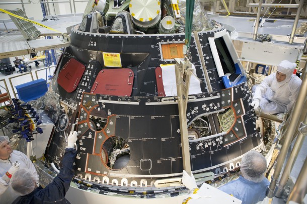 Inside the Operations and Checkout Building high bay at NASA's Kennedy Space Center in Florida, technicians dressed in clean-room suits install a back shell tile panel onto the Orion crew module. Image Credit: NASA/Dimitri Gerondidakis Inside the Operations and Checkout Building high bay at NASA's Kennedy Space Center in Florida, technicians dressed in clean-room suits install a back shell tile panel onto the Orion crew module. Image Credit: NASA/Dimitri Gerondidakis