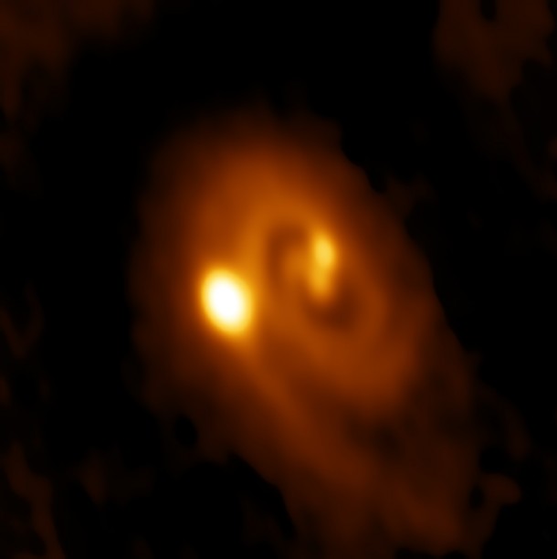 ALMA image of the L1448 IRS3B system, with two young stars at the center and a third distant from them. Spiral structure in the dusty disk surrounding them indicates instability in the disk, astronomers said. Credit: Bill Saxton, ALMA (ESO/NAOJ/NRAO), NRAO/AUI/NSF. ALMA image of the L1448 IRS3B system, with two young stars at the center and a third distant from them. Spiral structure in the dusty disk surrounding them indicates instability in the disk, astronomers said. Credit: Bill Saxton, ALMA (ESO/NAOJ/NRAO), NRAO/AUI/NSF.