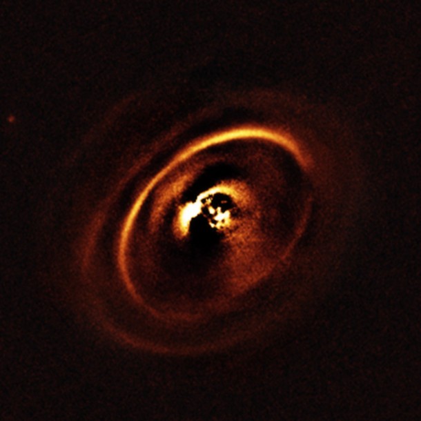 The central part of the image appears dark because SPHERE blocks out the light from the brilliant central star to reveal the much fainter structures surrounding it. Credit: ESO, J. de Boer et al. The central part of the image appears dark because SPHERE blocks out the light from the brilliant central star to reveal the much fainter structures surrounding it. Credit: ESO, J. de Boer et al.