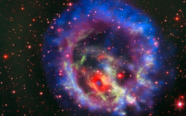 The reddish background image comes from the NASA/ESA Hubble Space Telescope and reveals the wisps of gas forming the supernova remnant 1E 0102.2-7219 in green. The red ring with a dark centre is from the MUSE instrument on ESO’s Very Large Telescope and the blue and purple images are from the NASA Chandra X-Ray Observatory. The blue spot at the centre of the red ring is an isolated neutron star with a weak magnetic field, the first identified outside the Milky Way. Credit: ESO/NASA, ESA and the Hubble Heritage Team (STScI/AURA)/F. Vogt et al. The reddish background image comes from the NASA/ESA Hubble Space Telescope and reveals the wisps of gas forming the supernova remnant 1E 0102.2-7219 in green. The red ring with a dark centre is from the MUSE instrument on ESO’s Very Large Telescope and the blue and purple images are from the NASA Chandra X-Ray Observatory. The blue spot at the centre of the red ring is an isolated neutron star with a weak magnetic field, the first identified outside the Milky Way. Credit: ESO/NASA, ESA and the Hubble Heritage Team (STScI/AURA)/F. Vogt et al.